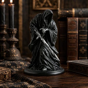 May include: A black figurine of a hooded, cloaked figure with skeletal hands gripping a silver sword. The figure is positioned in a kneeling stance on a circular base, featuring detailed fabric folds and a dark, weathered texture throughout the piece.
