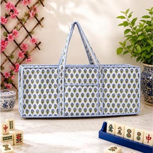 Könnte beinhalten: Eine rechteckige Stofftasche mit einem sich wiederholenden blau-grünen Blumenmuster auf weißem Grund, mit passender blau-weiß gestreifter Einfassung und zwei aufrechten Tragegriffen, konzipiert für den Transport von Mahjong-Spielsteinen.