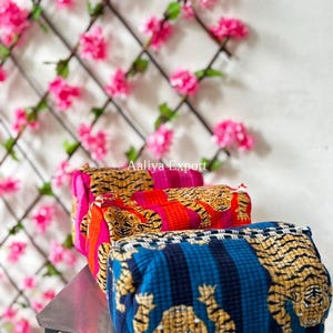 Könnte beinhalten: Drei rechteckige, gesteppte Taschen in einer Reihe, jede mit einem Tigerdruckmuster. Die vordere Tasche ist blau mit schwarzen Streifen, die mittlere ist rot mit schwarzen Streifen und die hintere ist rosa mit schwarzen Streifen. Der Text Aaliya Export ist sichtbar.