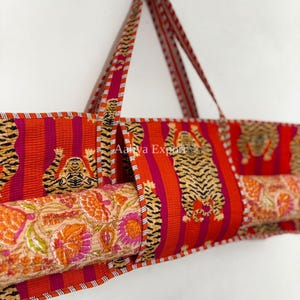 Può includere: Una borsa in tessuto trapuntato per tappetino da yoga con un vivace motivo a righe arancioni e magenta e illustrazioni di tigri ripetute. La borsa include lunghi manici e una fodera interna a contrasto con stampa floreale e il testo Aalya Export.