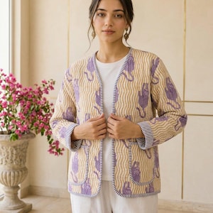 May include: A quilted jacket featuring a beige and white wavy line pattern with purple tiger motifs. The jacket has long sleeves with striped cuffs, an open front, and two front patch pockets, all finished with a dark blue and white striped trim.