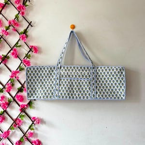 May include: A rectangular quilted tote bag featuring a repeating blue and green floral block print pattern on a white background. The bag has two matching fabric handles and blue and white striped piping along all edges and the central pocket.