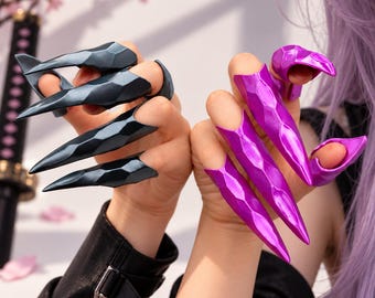 May include: A set of finger armor rings featuring a faceted, claw-like design. One hand wears four matte black rings, while the other hand wears four metallic magenta rings. Each ring covers the finger with a sharp, pointed tip.