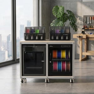 May include: A mobile workstation featuring a 3D printer on the left and a filament storage cabinet on the right. Two multi-spool units sit on top. The printer has a dark frame and glass door, while the cabinet displays colourful filament rolls.