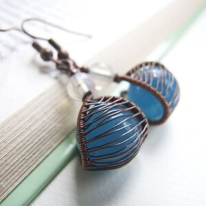 Peut inclure: Une paire de boucles d'oreilles en pierre bleue avec du fil de cuivre enroulé autour des pierres. Les boucles d'oreilles sont suspendues à des crochets en fil de cuivre.