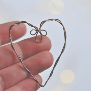 May include: A handcrafted copper wire heart with a delicate bow detail at the top. The heart shape is formed from twisted wire, creating a textured appearance. The background is blurred, highlighting the heart's intricate design.