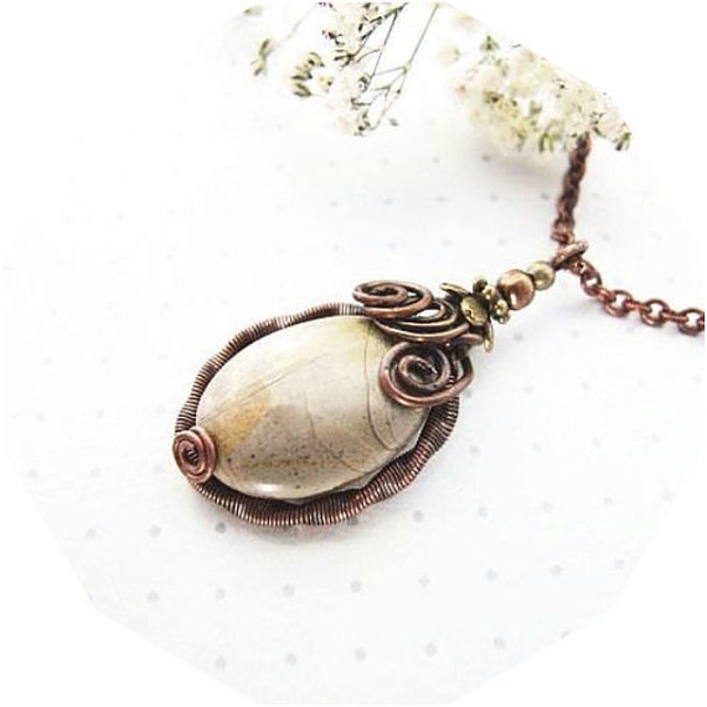 May include: A copper wire wrapped pendant featuring a light brown oval stone with brown and white swirls. The pendant is attached to a copper chain.
