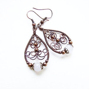 May include: A pair of copper wire earrings with a delicate, intricate design. Each earring features a teardrop shape with a white stone at the bottom.