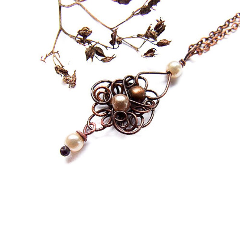 May include: A copper wire necklace with a delicate pendant featuring a swirl design and three white pearls.