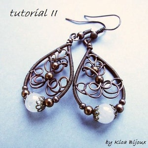 May include: A pair of copper wire earrings with a teardrop shape and a white stone bead at the bottom. The earrings are decorated with intricate wirework and have a delicate, feminine design.