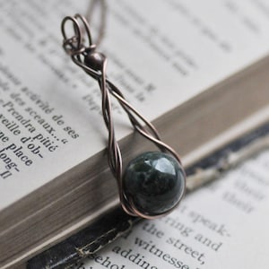 Puede incluir: Un collar con un colgante de alambre de cobre envuelto con una cuenta de ágata verde.