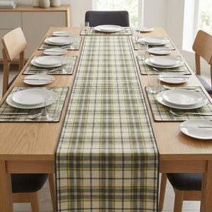 Puede incluir: Una mesa de comedor rectangular con un camino de mesa largo con un patrón de cuadros en tonos crema, verde oliva y gris carbón. La mesa está dispuesta con manteles individuales a juego, platos de cerámica blanca, vasos y cubiertos de plata.