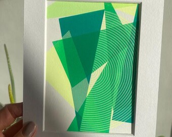 Könnte beinhalten: Abstrakter Kunstdruck mit weißem Passepartout und Rahmen. Der Druck zeigt überlappende geometrische Formen in Grün- und Gelbtönen.