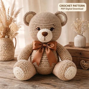 Könnte beinhalten: Ein hellbrauner Häkel-Teddybär mit cremefarbener Schnauze und Innenohren, dunklen Sicherheitsaugen, gestickter Nase und einer großen braunen Satinschleife um den Hals. Der Text CROCHET PATTERN PDF Digital Download ist im Bild zu sehen.