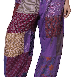 May include: Loose-fitting patchwork trousers featuring a variety of purple, maroon, and tan fabric panels with diverse floral, striped, and geometric patterns. The trousers include an elasticated drawstring waistband and gathered elastic ankle cuffs.