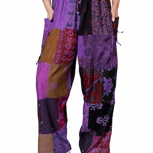 Puede incluir: Pantalones de estilo patchwork con corte holgado, confeccionados con paneles de tela en tonos morado, negro y marrón que presentan diversos estampados, incluyendo elefantes, cachemir y motivos florales. Tienen cintura elástica con cordón y bolsillos.