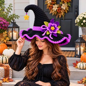 May include: A black crocheted witch hat featuring a purple band, a wavy purple brim edge, and a large purple and green crocheted flower accent. A small yellow crocheted star charm hangs from the pointed tip of the hat by a thin black cord.