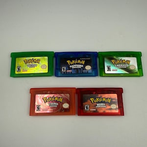 May include: Five rectangular video game cartridges for a handheld console. The top row features green LeafGreen, blue Sapphire, and green Emerald versions. The bottom row features orange FireRed and red Ruby versions, all with Pok&eacute;mon branding.