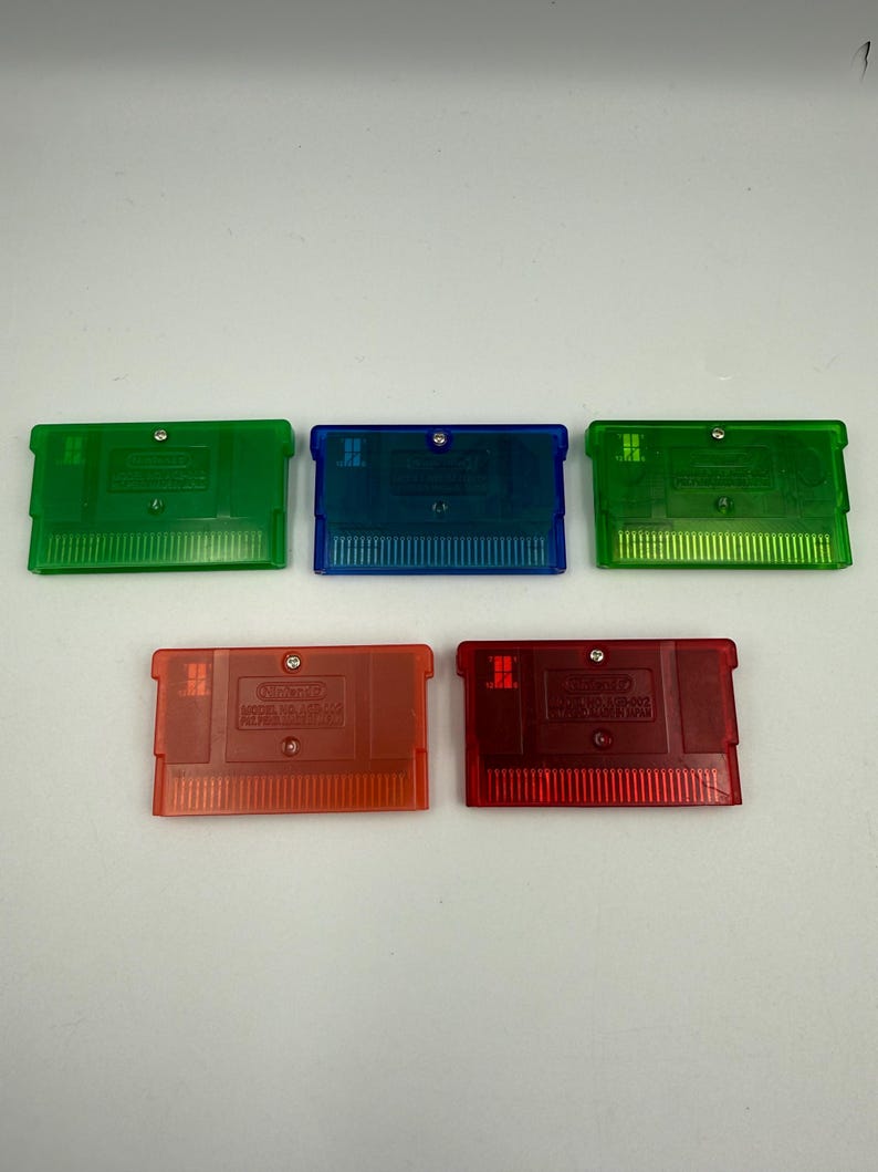 May include: Five rectangular video game cartridges with translucent plastic shells. The collection includes two green, one blue, and two red cartridges. Each unit features a metallic screw, a connector edge, and embossed Nintendo branding text.