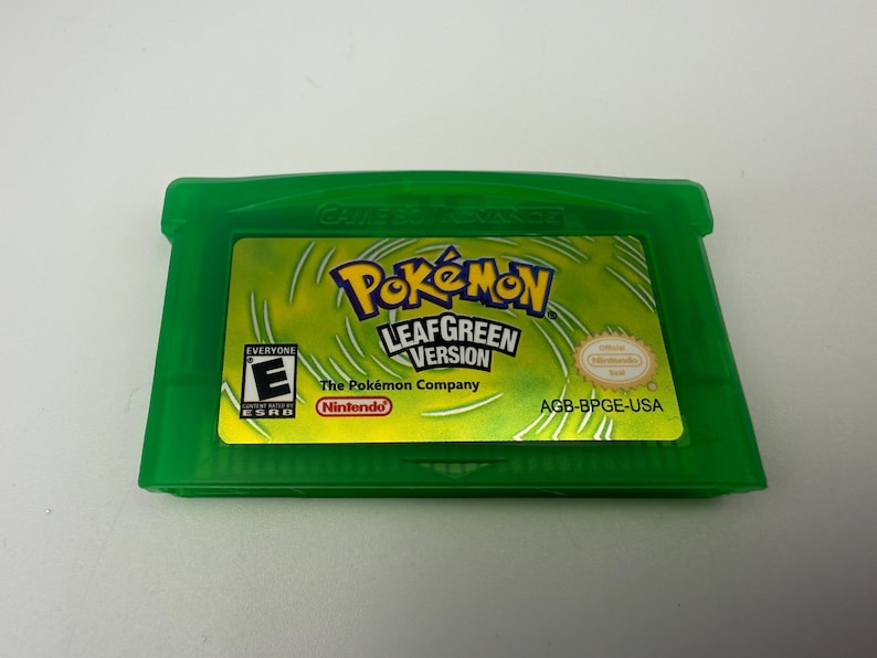 May include: A translucent green Game Boy Advance video game cartridge for Pok&eacute;mon LeafGreen Version. The label features the Pok&eacute;mon logo, the text LeafGreen Version, an ESRB E rating, the Nintendo logo, and the product code AGB-BPGE-USA.