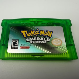May include: A translucent green Game Boy Advance video game cartridge for Pok&eacute;mon Emerald Version. The label features the game title, the ESRB E rating, the Nintendo logo, and the text AGB BPEE-USA printed on a silver background.