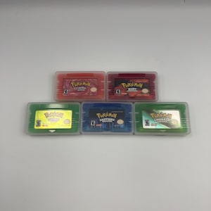 May include: Five Nintendo Game Boy Advance video game cartridges in clear plastic protective cases. The titles include Pok&eacute;mon FireRed, Ruby, LeafGreen, Sapphire, and Emerald versions, each featuring its respective colorful label and logo.