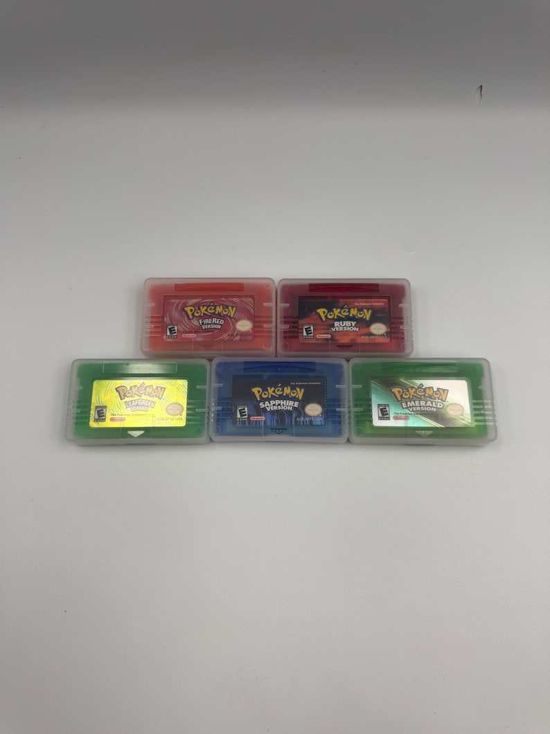 May include: Five Nintendo Game Boy Advance video game cartridges in clear plastic protective cases. The titles include Pok&eacute;mon FireRed, Ruby, LeafGreen, Sapphire, and Emerald versions, each featuring its respective colorful label and logo.