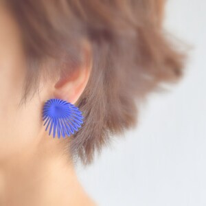 May include: A close-up of a person's ear wearing a blue, geometric, fan-shaped earring.