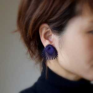May include: A pair of purple, geometric earrings with a sunburst design. The earrings are made of metal and have a shiny finish.
