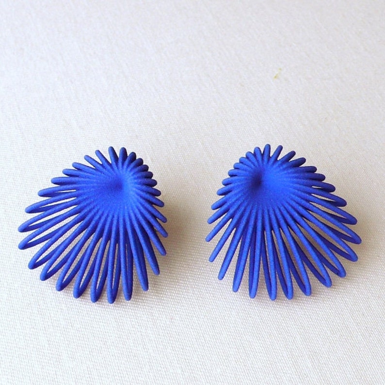 May include: A pair of blue earrings with a unique, geometric design. The earrings are made of metal and have a starburst shape.