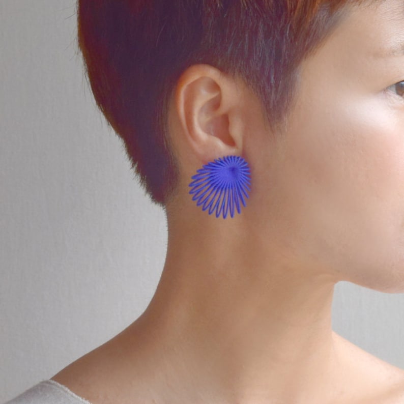 May include: A pair of blue earrings with a geometric, fan-shaped design. The earrings are made of a thin, wire-like material.