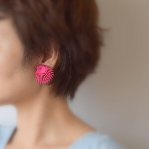 May include: A close-up of a person's ear with a pink, geometric, fan-shaped earring.