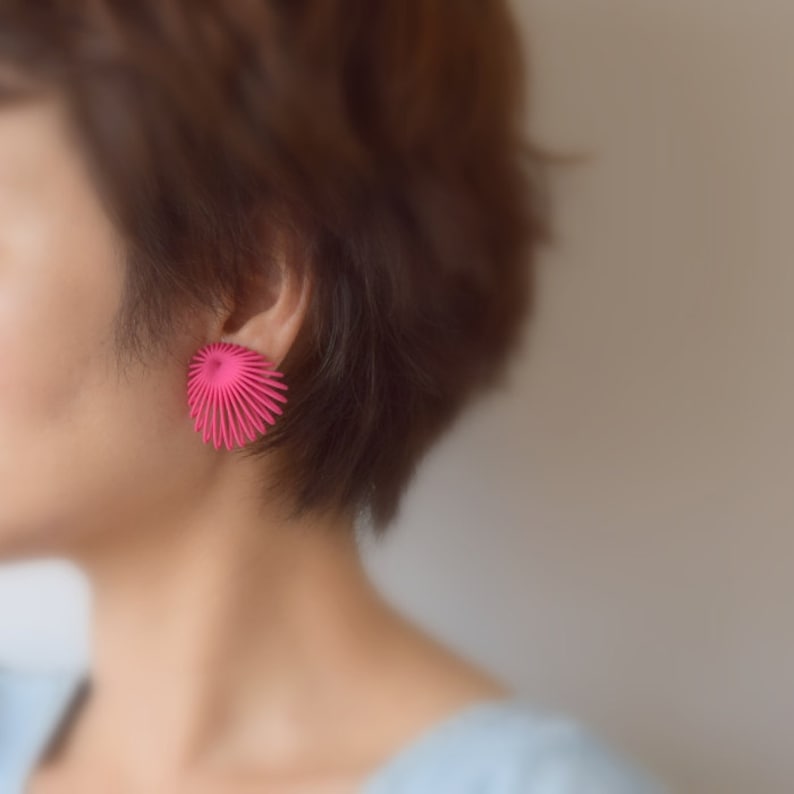 May include: A close-up of a person's ear with a pink, geometric, fan-shaped earring.