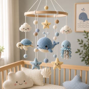 May include: A nursery mobile featuring a circular wooden frame with hanging crochet figures including a blue whale, a turtle, a jellyfish, clouds, stars, a seashell, and small spheres in shades of blue, cream, and tan, all with embroidered faces.