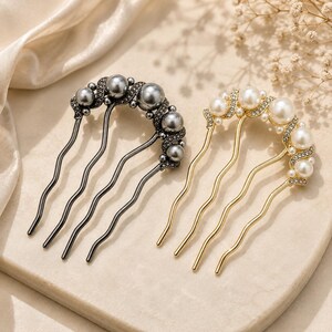 May include: Two hair combs with wavy prongs, one in a dark gunmetal finish with grey faux pearls and one in a gold finish with white faux pearls. Both combs feature a curved top edge adorned with small clear crystals and multiple round pearls.