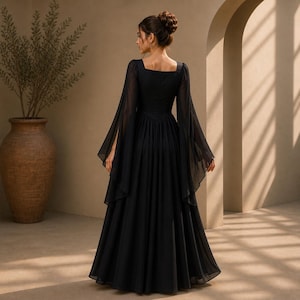 May include: A floor-length black dress featuring a square neckline and long, flowing bell sleeves. The garment has a fitted bodice that transitions into a full, pleated skirt made of a sheer, lightweight fabric that drapes to the floor.