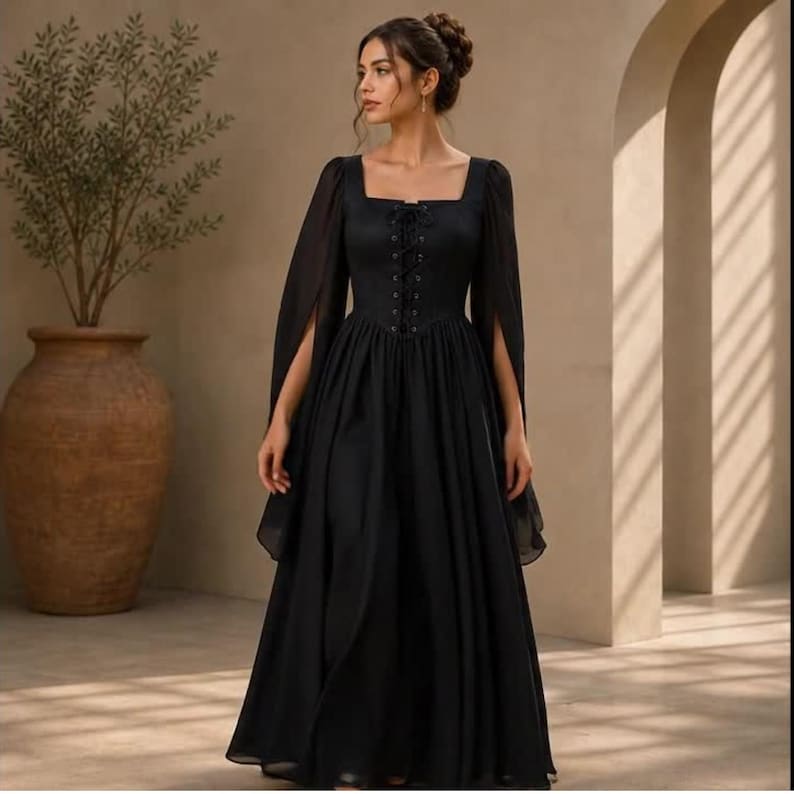 May include: A floor-length black dress featuring a square neckline, a lace-up corset-style bodice with vertical eyelets, and long, flowing sheer sleeves. The skirt is full and gathered at the waist, creating a voluminous silhouette in solid black.