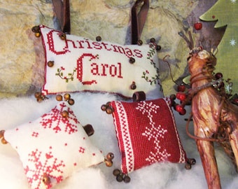 Pode incluir: Três almofadas de Natal bordadas em branco e vermelho com desenhos de flocos de neve. As almofadas são decoradas com contas de madeira. Uma almofada tem o texto "Christmas Carol" bordado.