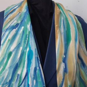May include: A blue, green, and beige patterned silk scarf. The scarf is draped over a blue blazer.