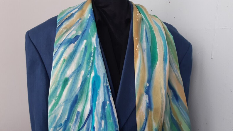 May include: A blue, green, and beige patterned silk scarf. The scarf is draped over a blue blazer.