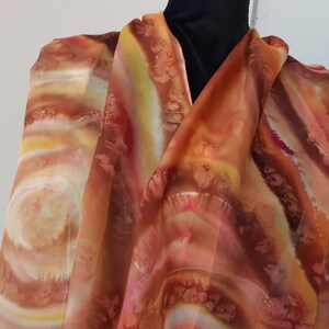 May include: A long, rectangular, orange, yellow, and brown silk scarf with a swirling, abstract pattern.