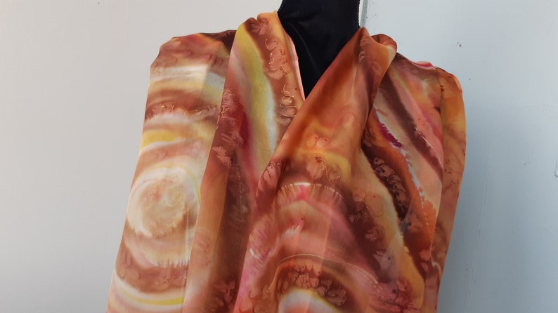 May include: A long, rectangular, orange, yellow, and brown silk scarf with a swirling, abstract pattern.