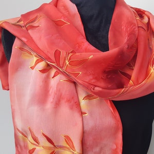 May include: A red silk scarf with a floral pattern in shades of orange and yellow. The scarf is draped over a black mannequin.
