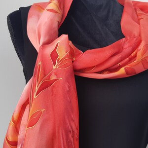 May include: A red silk scarf with a floral pattern in shades of orange and gold. The scarf is tied around a black shirt.