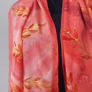 May include: A red silk scarf with a gold leaf design. The scarf is hand-painted and has a soft, flowing texture.