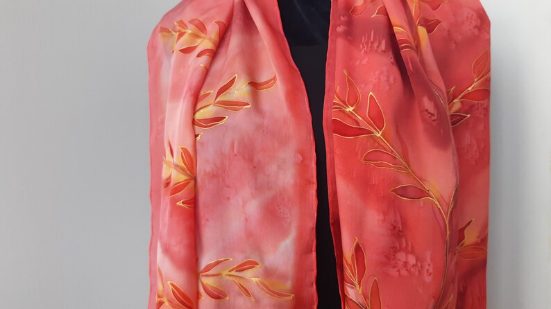 May include: A red silk scarf with a gold leaf design. The scarf is hand-painted and has a soft, flowing texture.