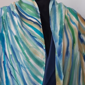 May include: A blue, green, and white silk scarf with a watercolor-like pattern. The scarf is draped over a mannequin's shoulders.