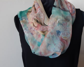 Puede incluir: Una bufanda transparente con un patrón floral en tonos de rosa, azul y verde. La bufanda está hecha de seda y tiene una textura delicada y fluida.