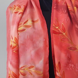 May include: A red silk scarf with a gold leaf design. The scarf is hand-painted and has a gradient of color from light pink to red.