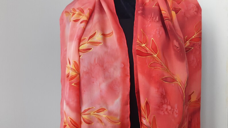 May include: A red silk scarf with a gold leaf design. The scarf is hand-painted and has a gradient of color from light pink to red.